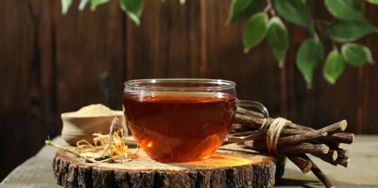 a cup of licorice tea with licorice roots on a rustic wooden surface.