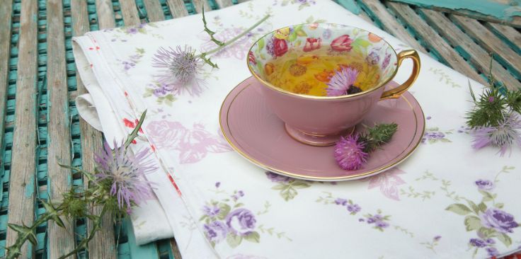 a floral tea cup with milk thistle flowers on a patterned cloth.