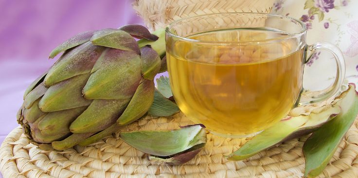 a glass cup of artichoke tea with fresh artichoke on a woven mat.