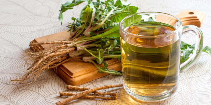 a glass mug of dandelion root tea with fresh dandelion roots and leaves.