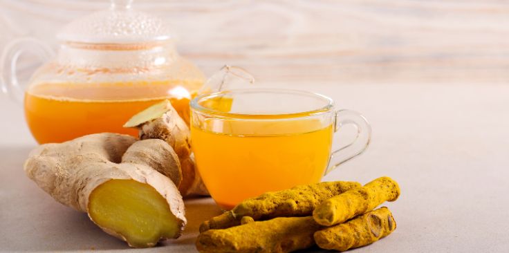 a glass teacup of turmeric tea with fresh turmeric and ginger roots.