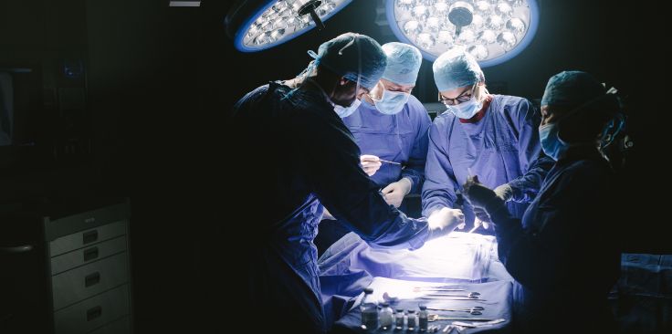 a team of surgeons performing an operation under bright surgical lights in an operating room.