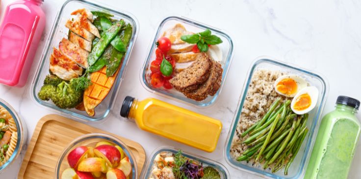 a person in a kitchen sealing glass meal prep containers filled with salmon, rice, and broccoli.