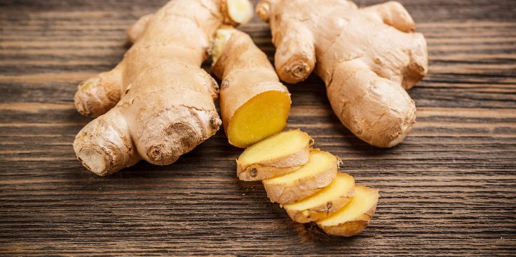 fresh ginger root with one root sliced, displayed on a wooden surface.