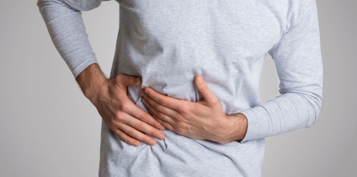 a man holding his right side in discomfort, indicating potential liver pain.