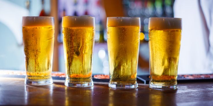 four pints of beer with frothy heads lined up on a bar counter.