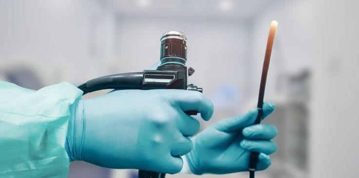 Doctor holding a colonoscopy device with gloved hands in a medical setting.