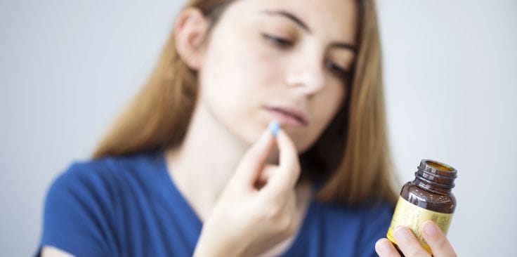 Woman reading a supplement label and holding a pill.