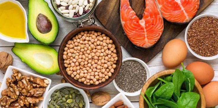 a variety of healthy foods including salmon, avocado, walnuts, and leafy greens arranged on a table.