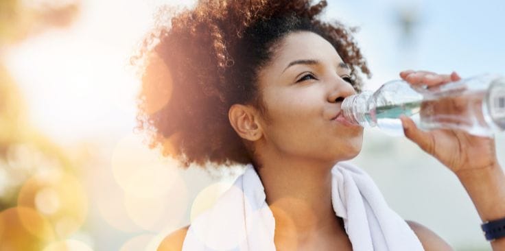 a woman staying hydrated by drinking water after exercise.