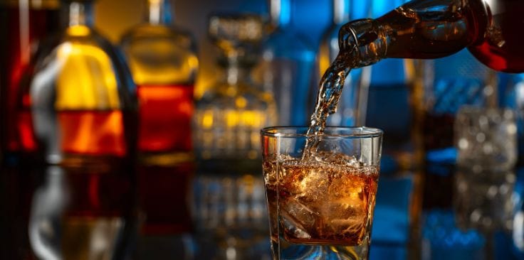 Alcohol being poured into a glass filled with ice