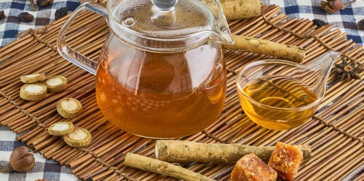 burdock root tea with fresh burdock roots and honey on a woven mat.