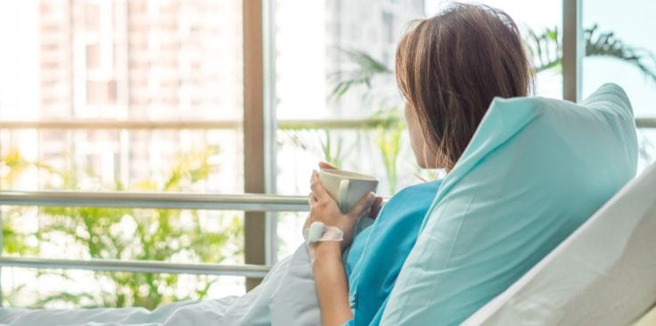 Patient resting in a hospital bed with a drink in hand.