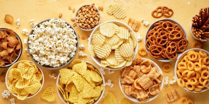 Assorted snacks, including chips and pretzels, on a yellow background.