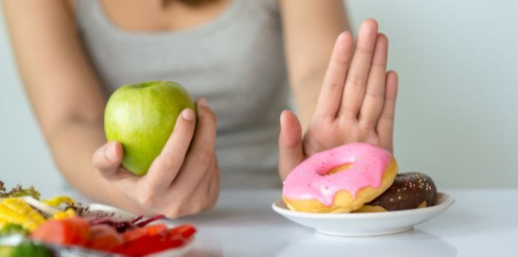 Person refusing donuts, choosing an apple instead, avoiding worst foods for the lymphatic system.