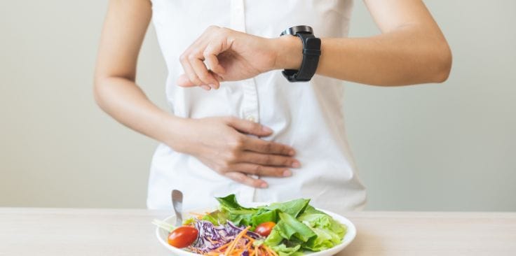 A person looking at their watch while eating a fresh salad, emphasizing mindful eating and timing in relation to turmeric benefits for overall well-being.