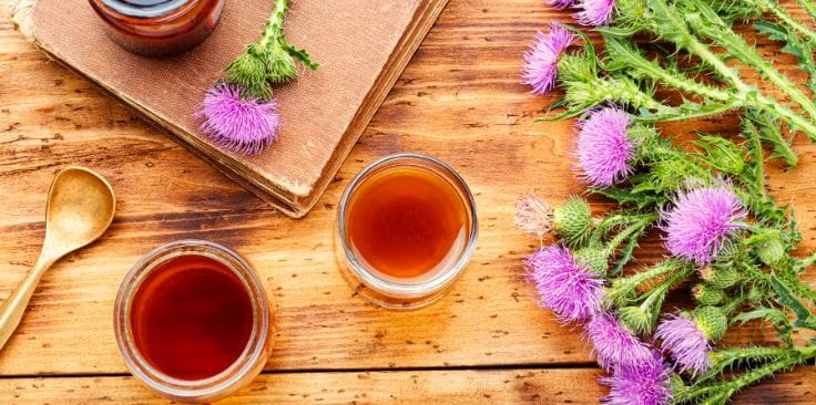 a wooden table with milk thistle flowers, herbal tonic in jars, and a golden spoon, showcasing natural liver health remedies. 