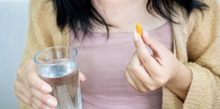 A woman holding a glass of water and a turmeric capsule, highlighting its convenience and potential benefits for skin and health.