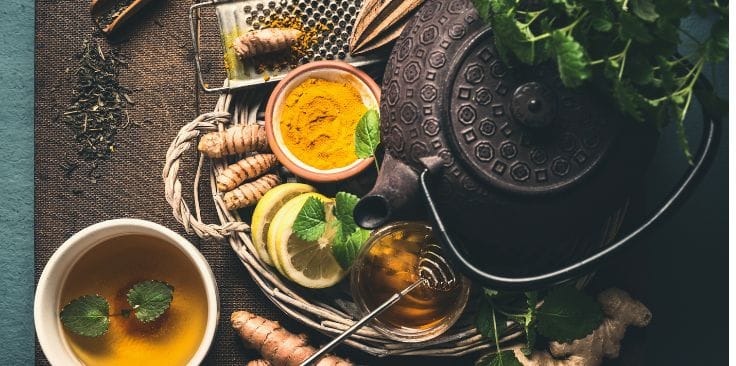 Ingredients for turmeric tea including fresh turmeric, lemon, honey, and a teapot in a cozy setup.