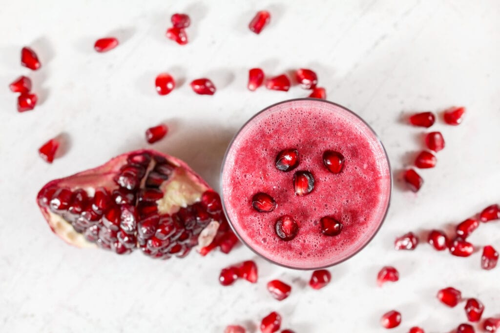 Image shows a red drink with pomegranate seeds on top of it