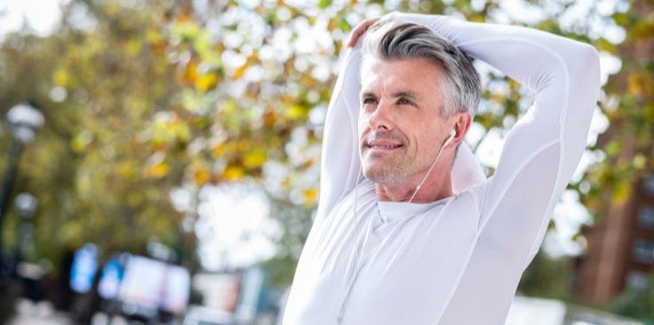 man stretching outdoors while listening to music with earphones in a park. 