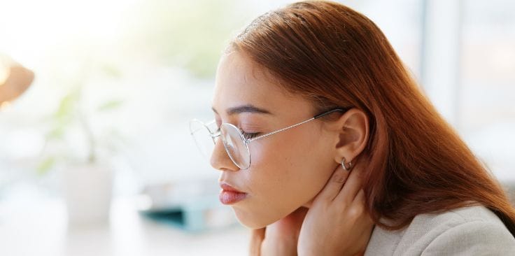 woman with glasses massaging her neck, likely due to swollen lymph nodes. 